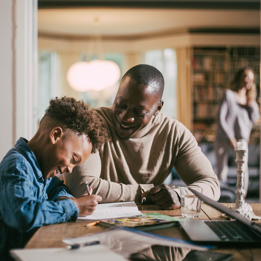 Person with their child smiling while doing homework.