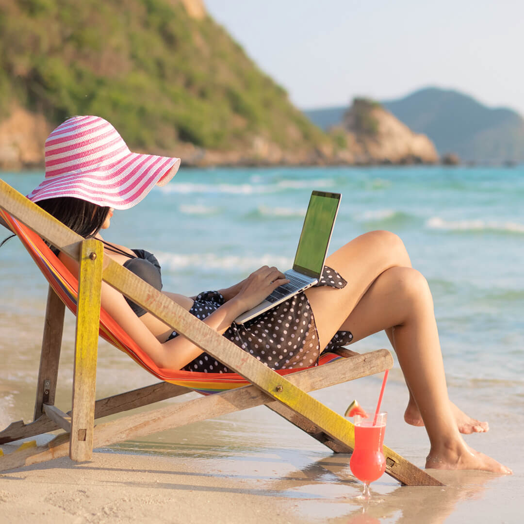 Person sitting on beach while working on their laptop.